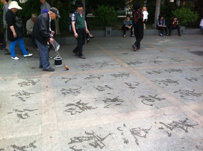 Un hombre escribe carácteres en el suelo con agua. Hangzhou (China).